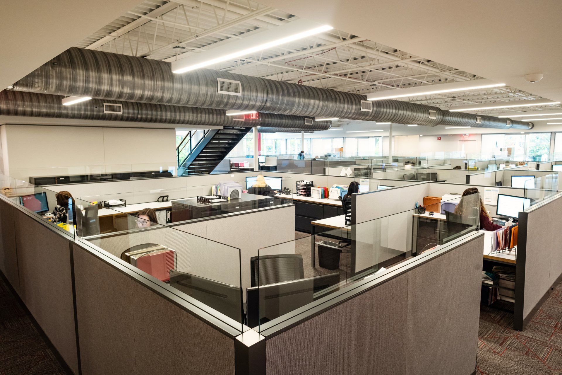 A large office with cubicles and a staircase in the background.