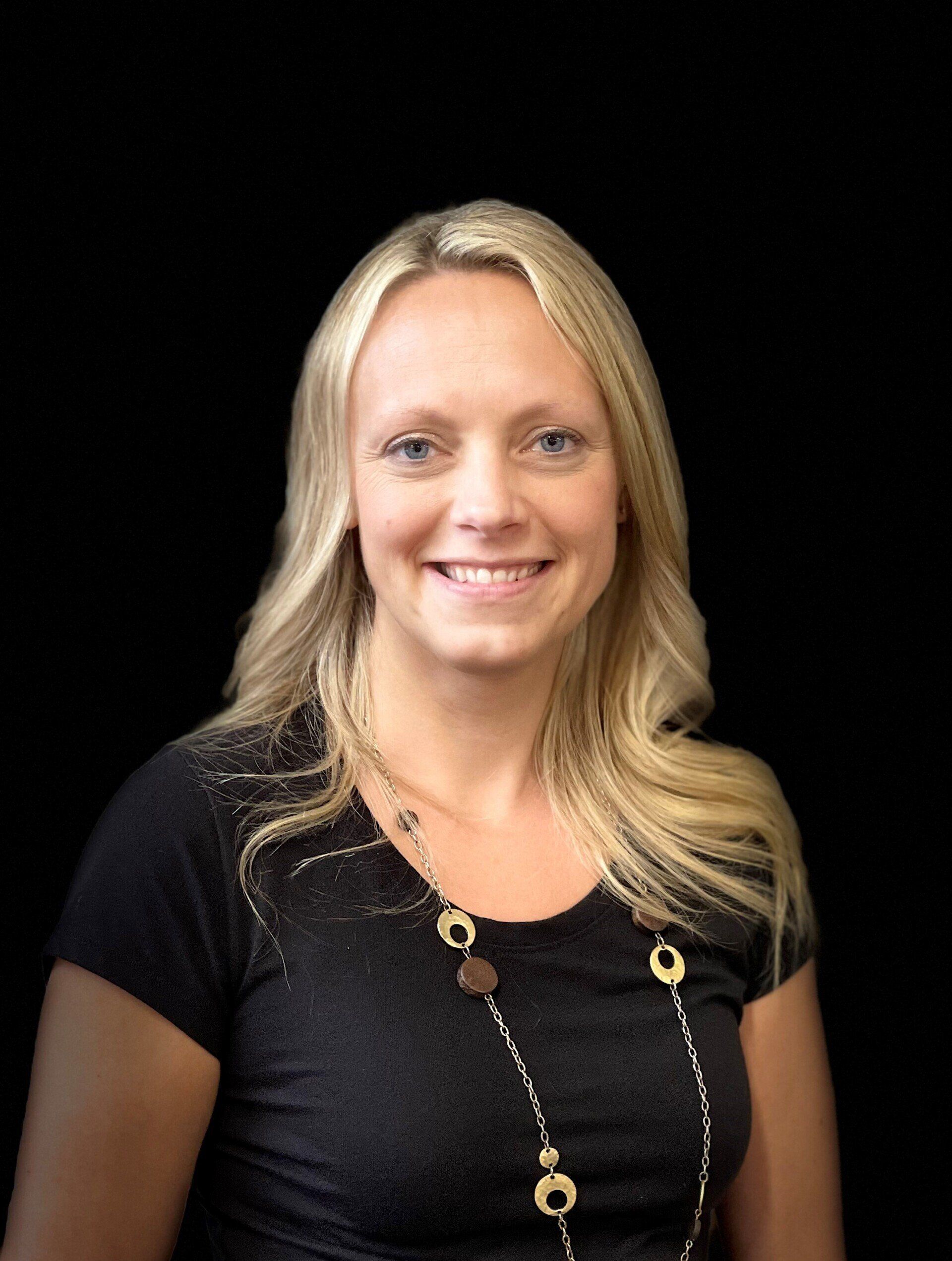 A woman wearing a black shirt and a necklace smiles for the camera
