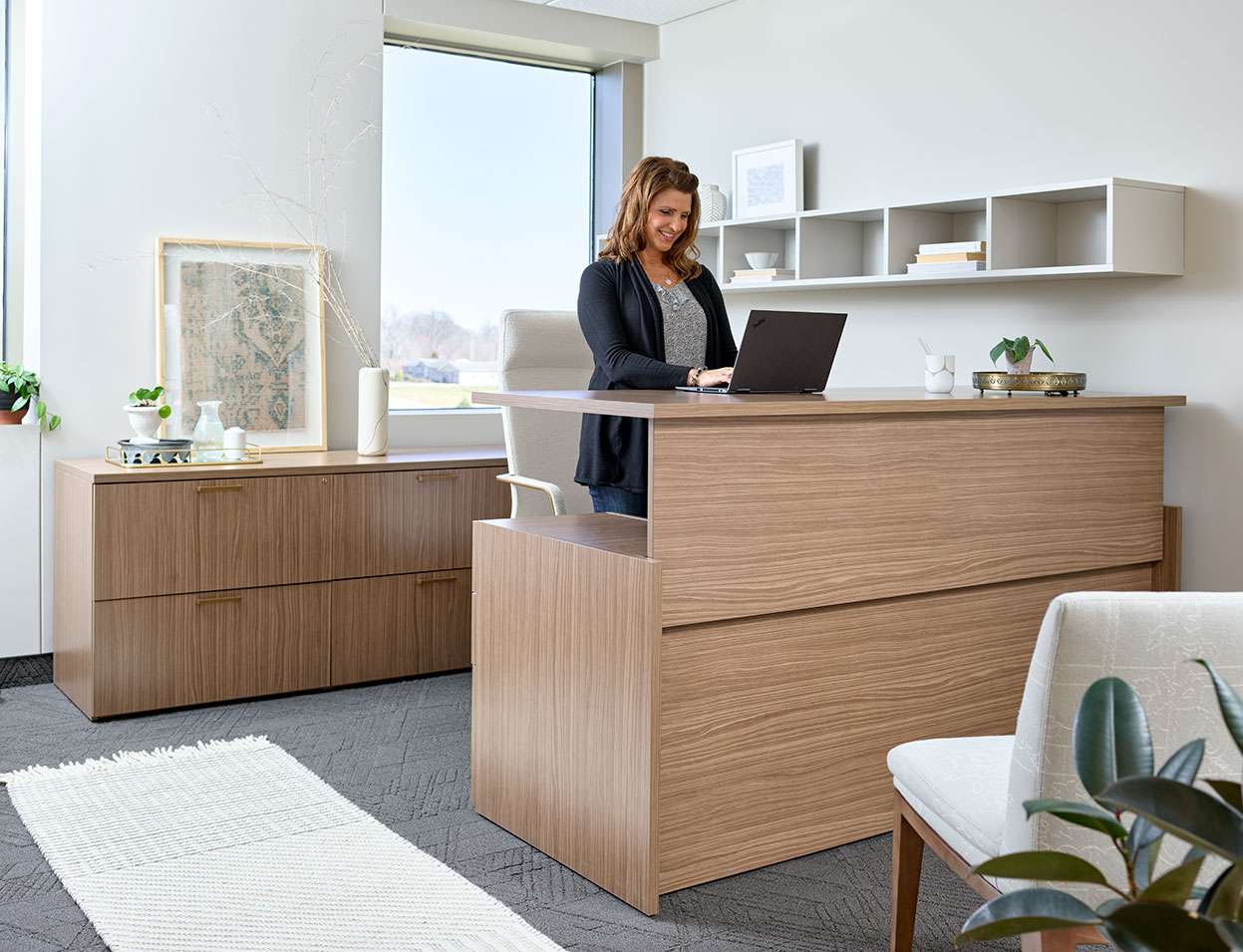A woman is standing at a desk using a laptop computer.