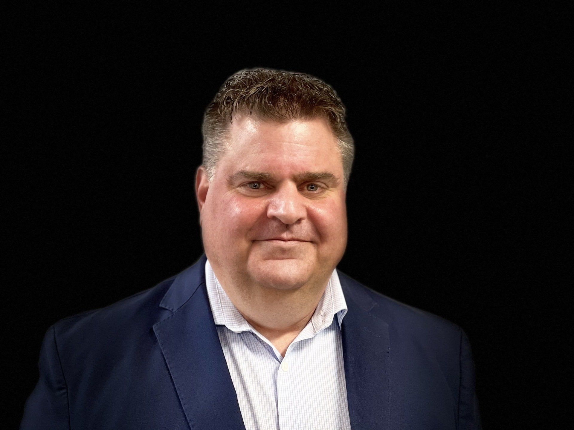 A man in a suit and white shirt is standing in front of a black background.