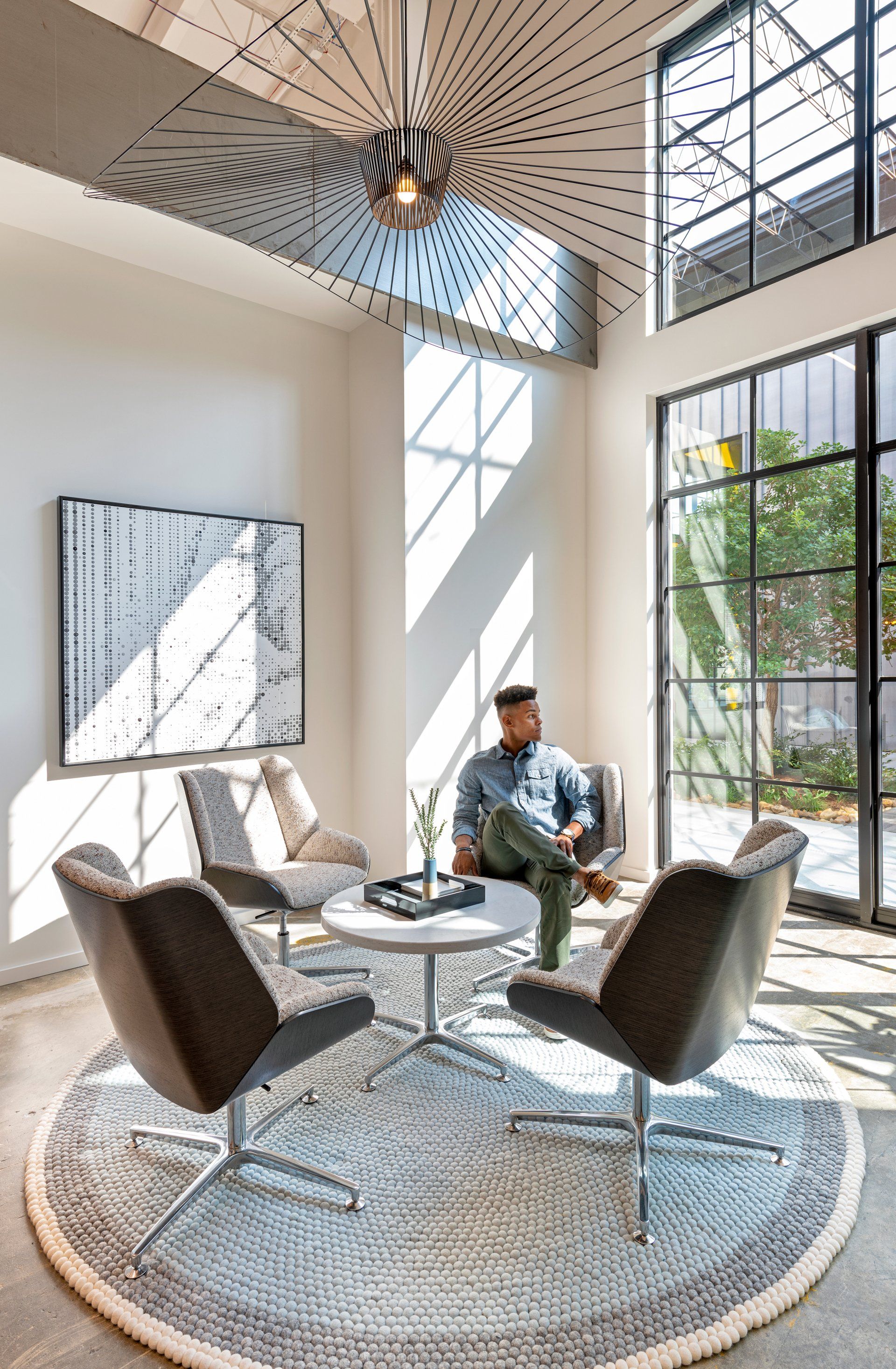 A man is sitting at a table in a living room surrounded by chairs.