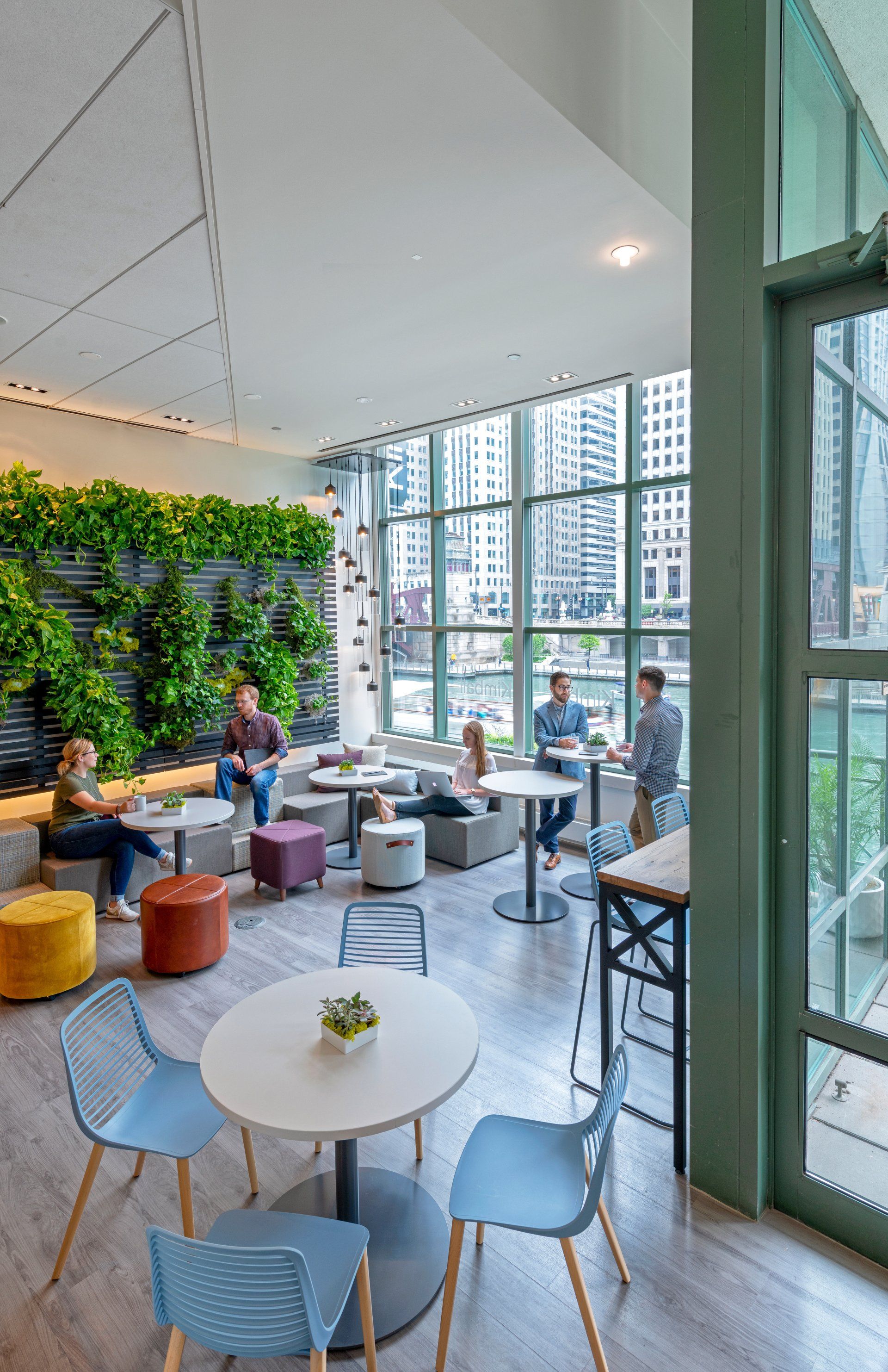 A group of people are sitting at tables in a room with lots of windows.