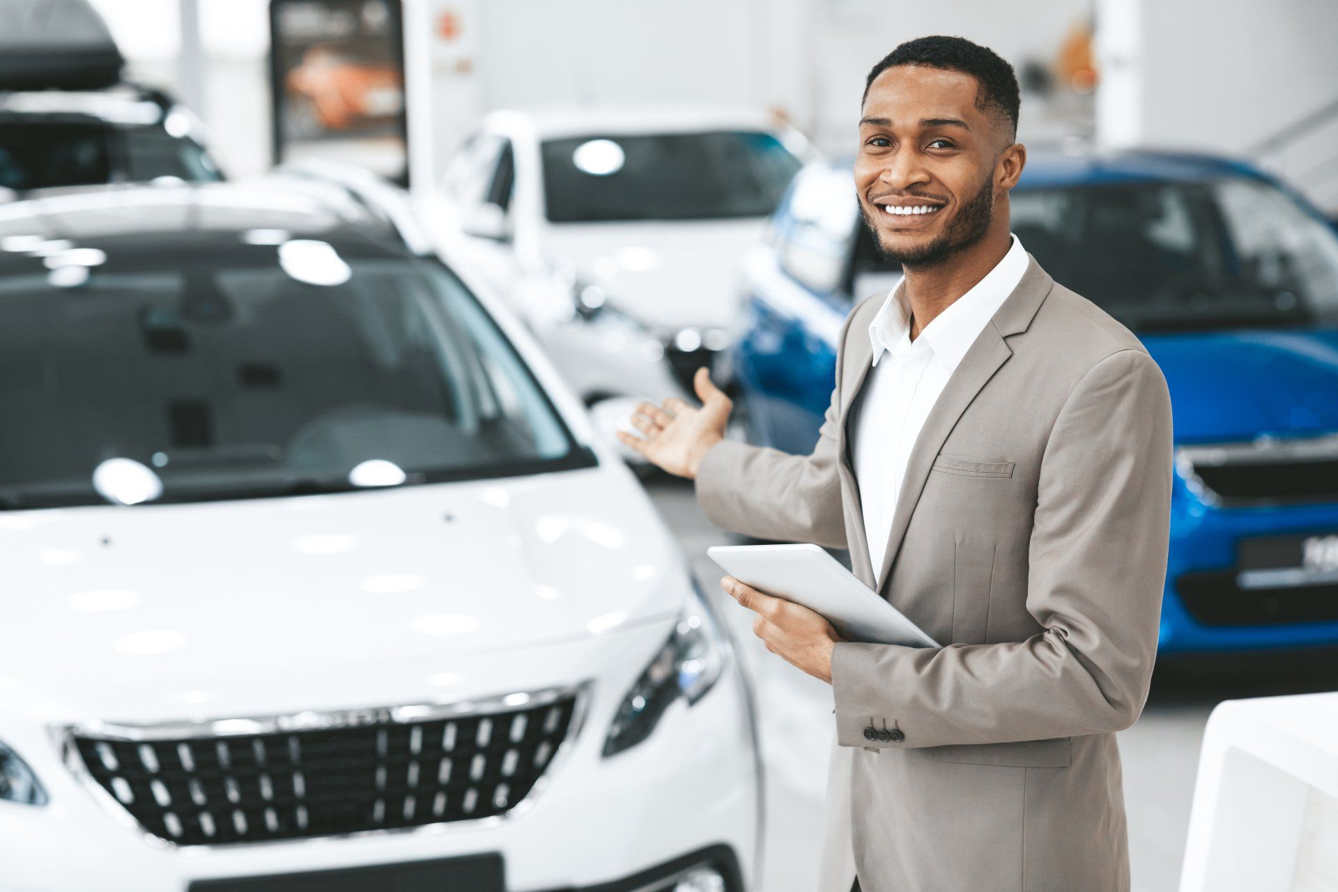 A man is holding a tablet in front of a car in a showroom.