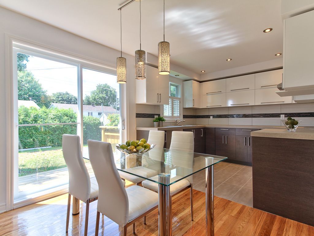 Cuisine moderne avec table en verre, chaises blanches, armoires marron et suspensions.