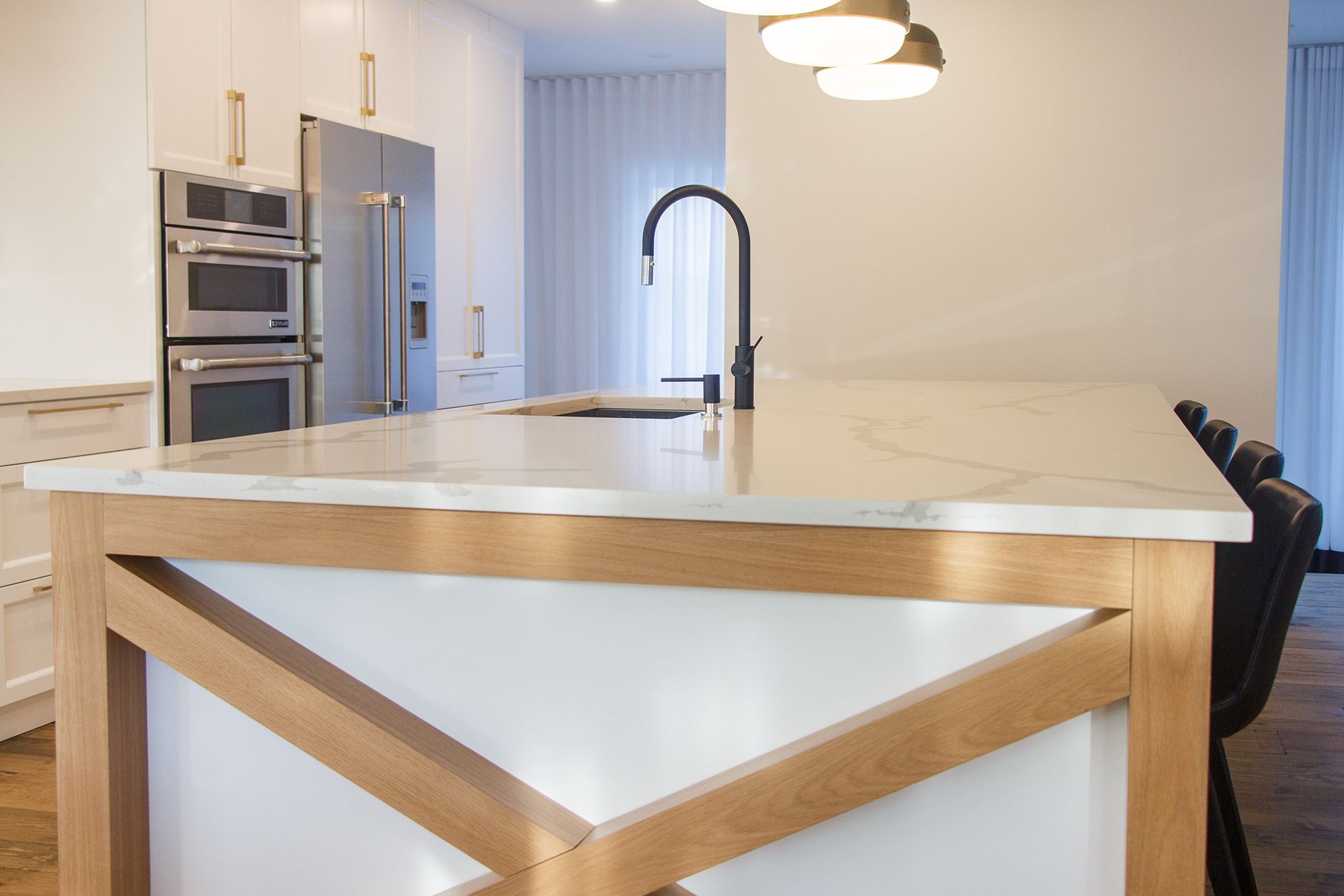 Cuisine moderne avec armoires en bois, touches de noir, électroménagers en acier inoxydable et éclairage sur rail.