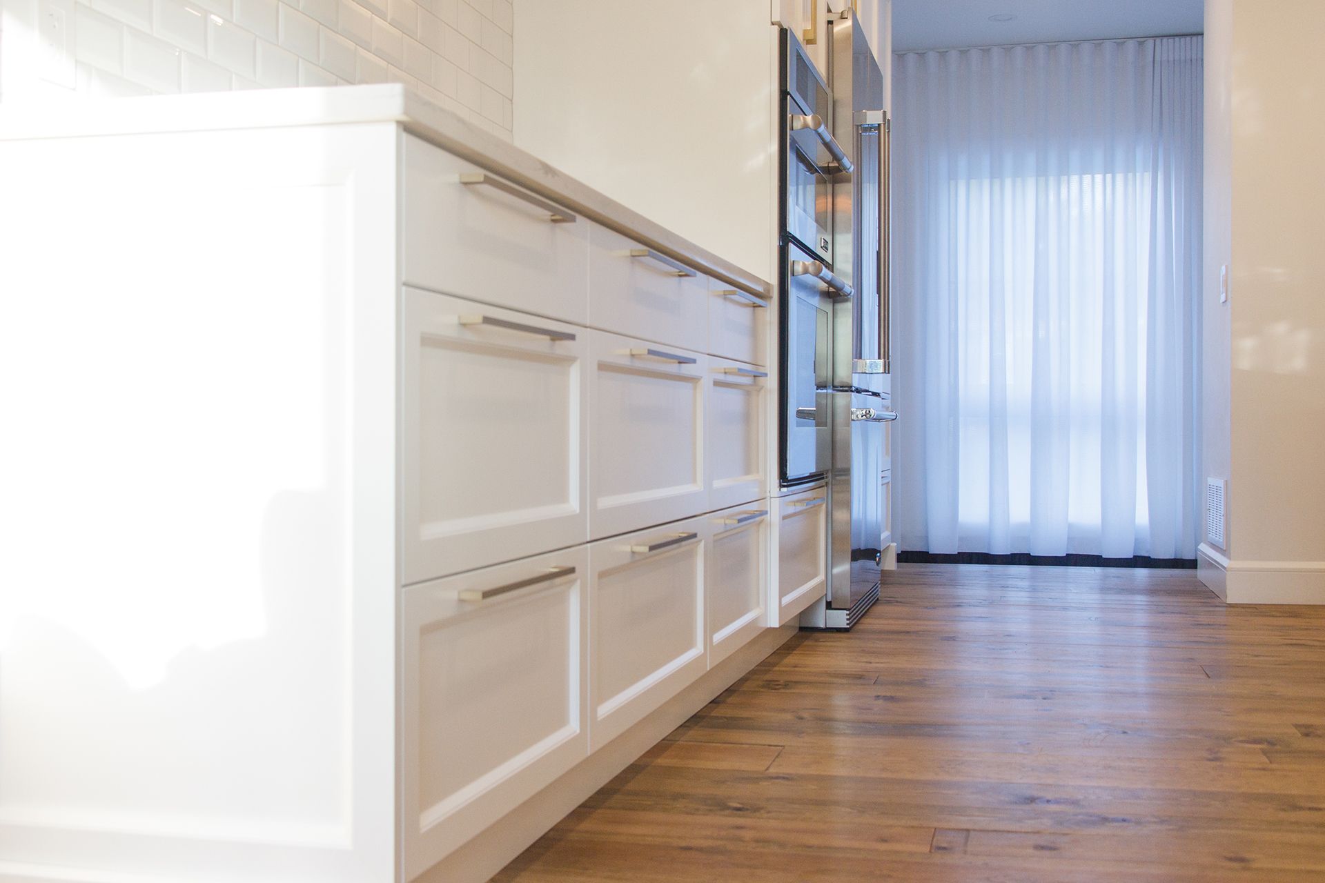 Une cuisine moderne avec des armoires blanches, des appareils électroménagers en acier inoxydable et un parquet