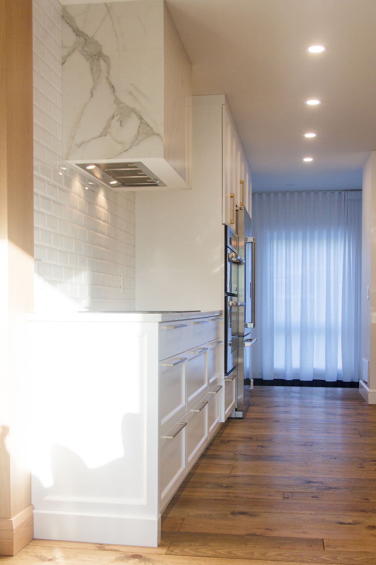 Une cuisine moderne avec des armoires blanches, une hotte aspirante revêtue de marbre, des carreaux de métro et un parquet.