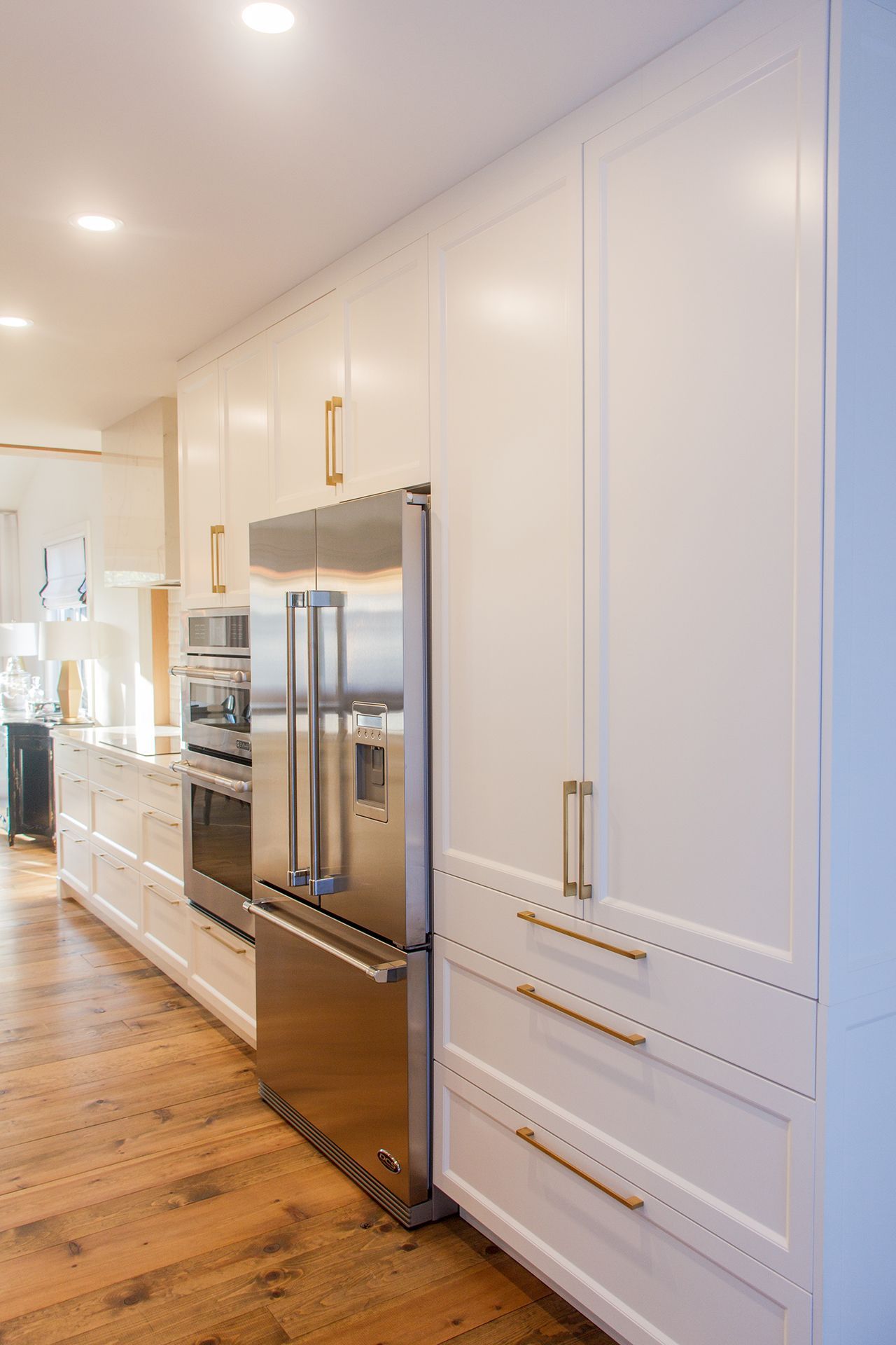 Cuisine équipée de placards blancs avec poignées dorées et réfrigérateur en acier inoxydable, le tout sur un parquet.