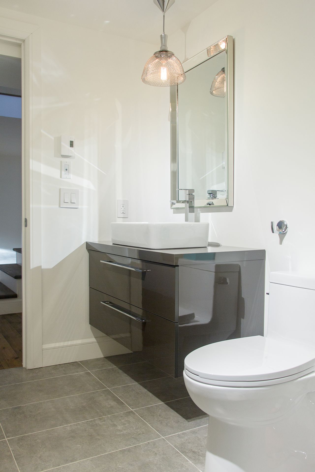 Une salle de bains moderne avec un lavabo vasque blanc sur un meuble-lavabo gris suspendu, une suspension lumineuse