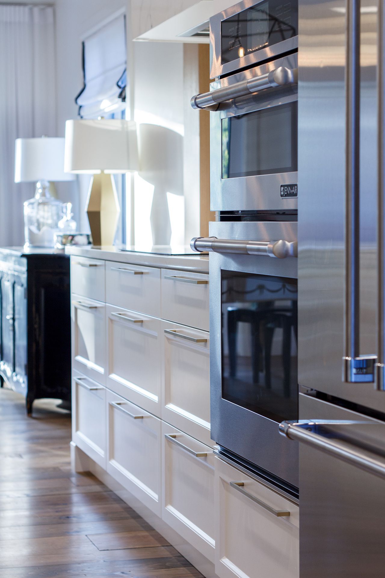 Une cuisine moderne avec des armoires blanches, des fours en acier inoxydable et une lampe dorée sur le comptoir.