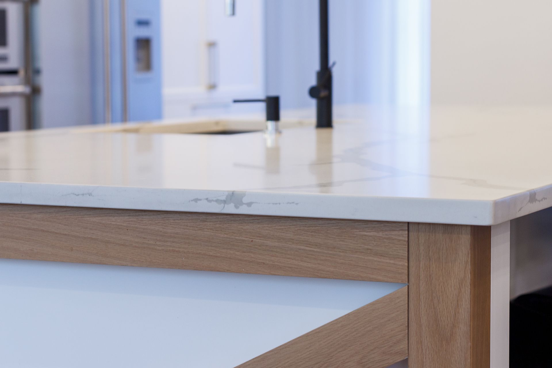 Un îlot de cuisine avec un plan de travail en marbre blanc et un socle en panneaux de bois, équipé d'un robinet noir moderne