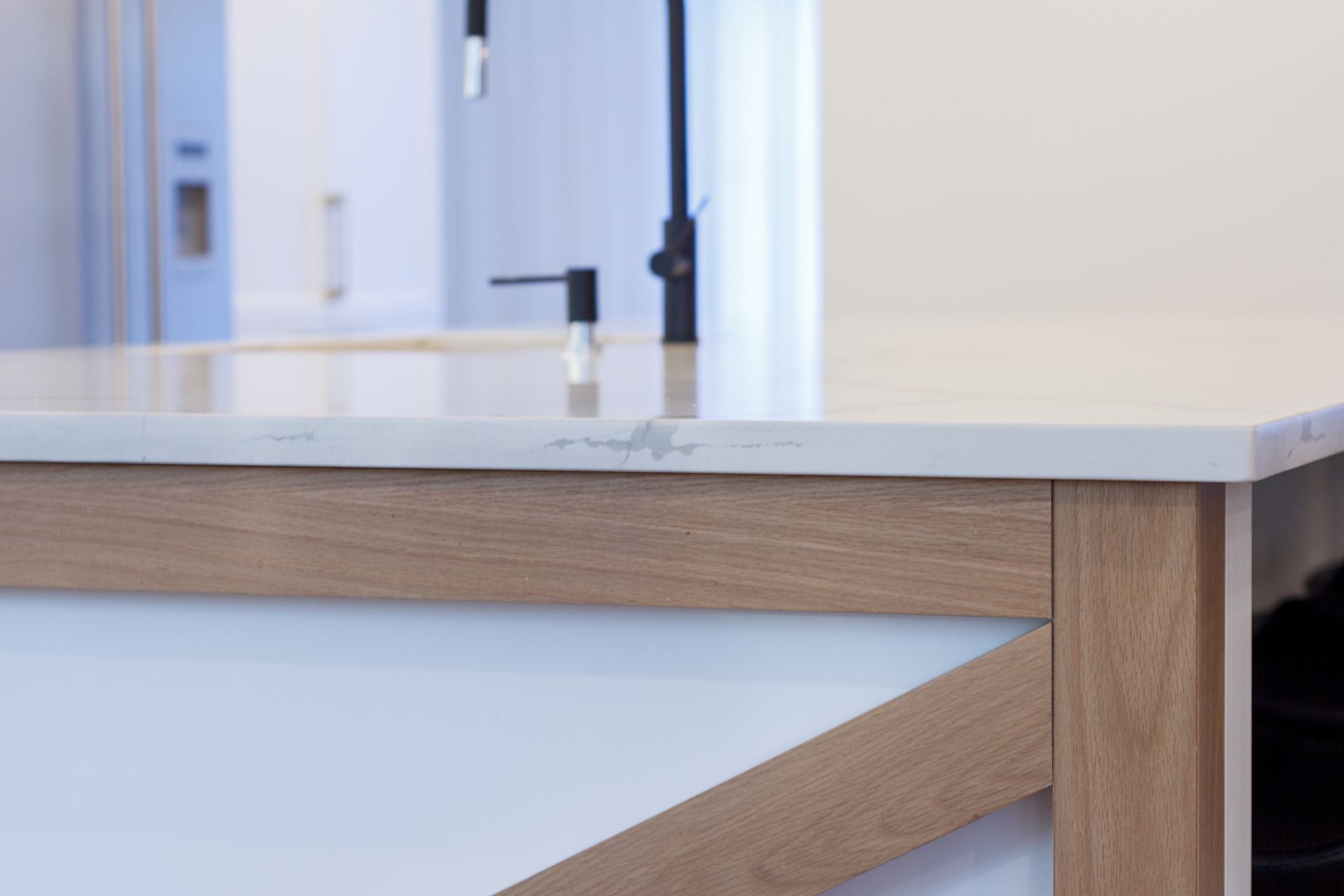 Gros plan sur un îlot de cuisine avec un plan de travail clair et une structure en bois ; un robinet noir est visible en arrière-plan.