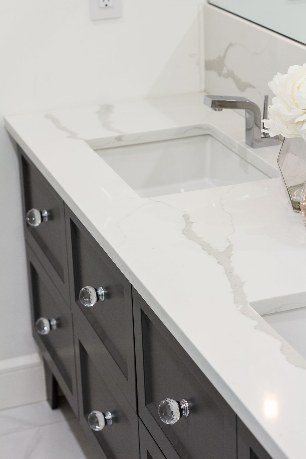 Meuble-lavabo gris foncé avec plan de travail blanc et vasque carrée. Poignées en cristal.