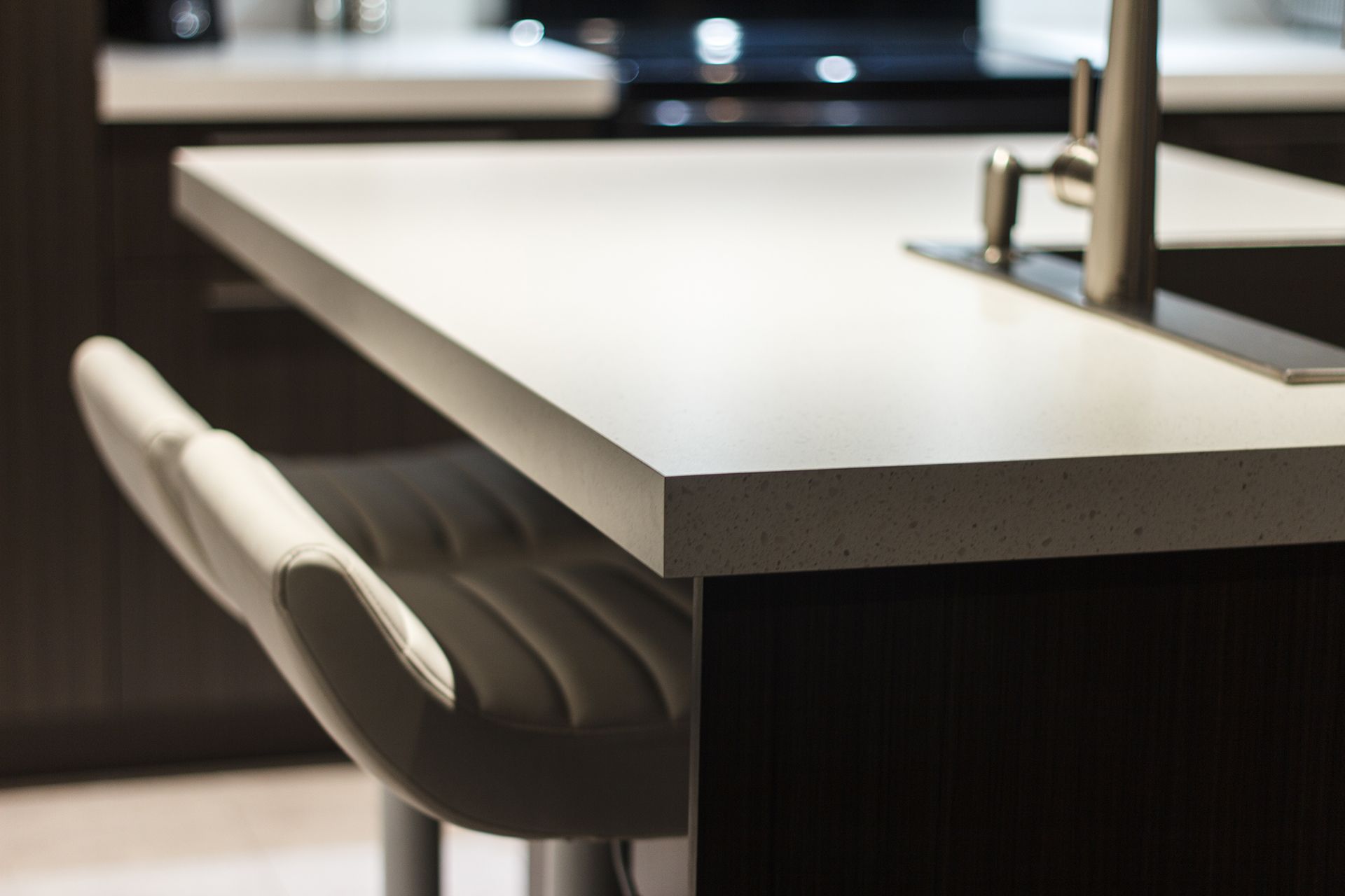 Gros plan d'un îlot de cuisine moderne avec un comptoir blanc et un tabouret de bar en cuir.