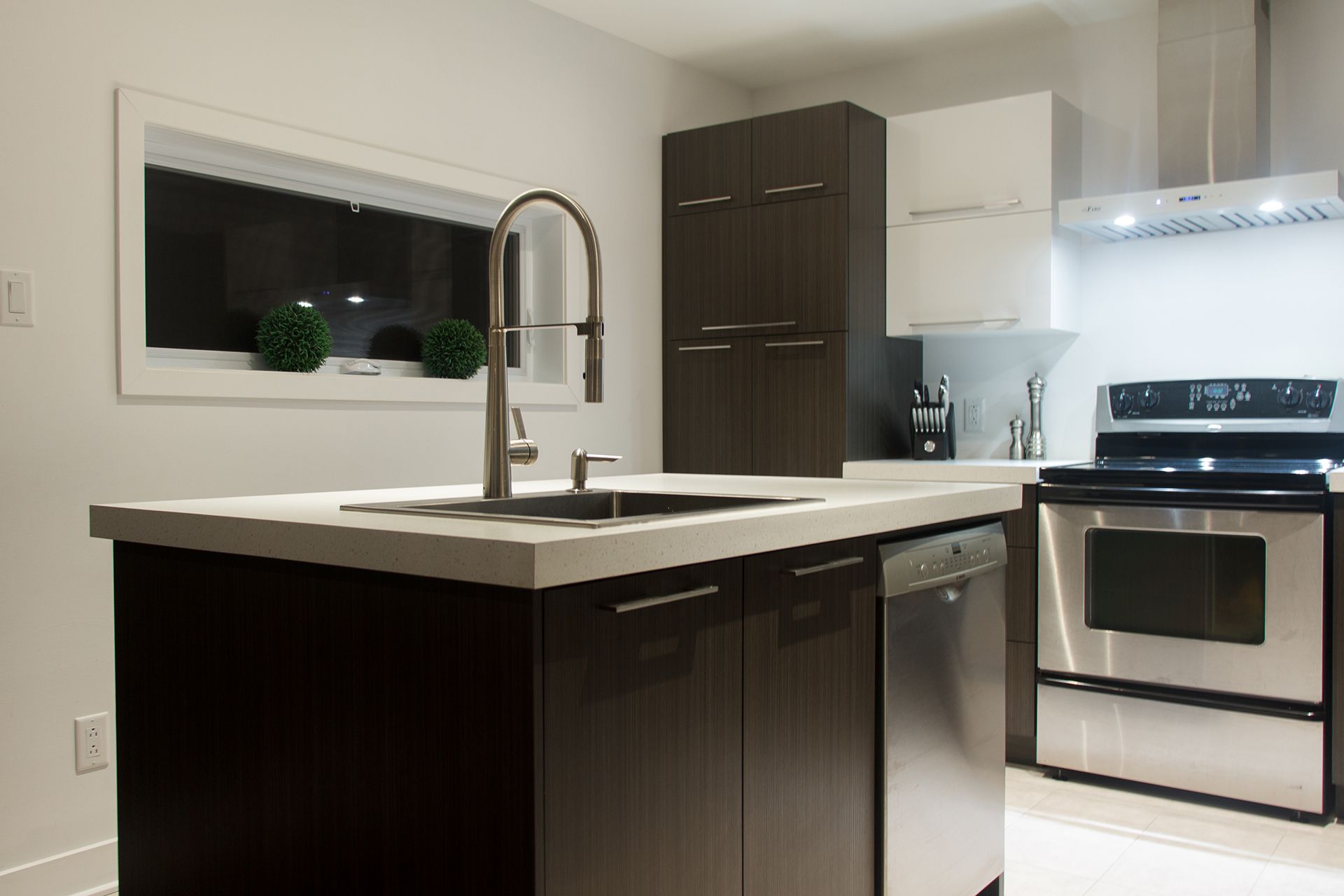 Cuisine moderne avec armoires foncées, appareils électroménagers en acier inoxydable et un îlot central avec évier.