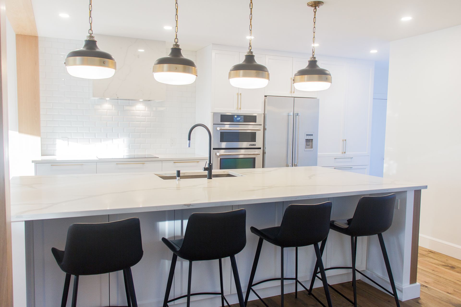 Cuisine moderne avec îlot, luminaires suspendus, électroménagers en acier inoxydable et tabourets de bar noirs.