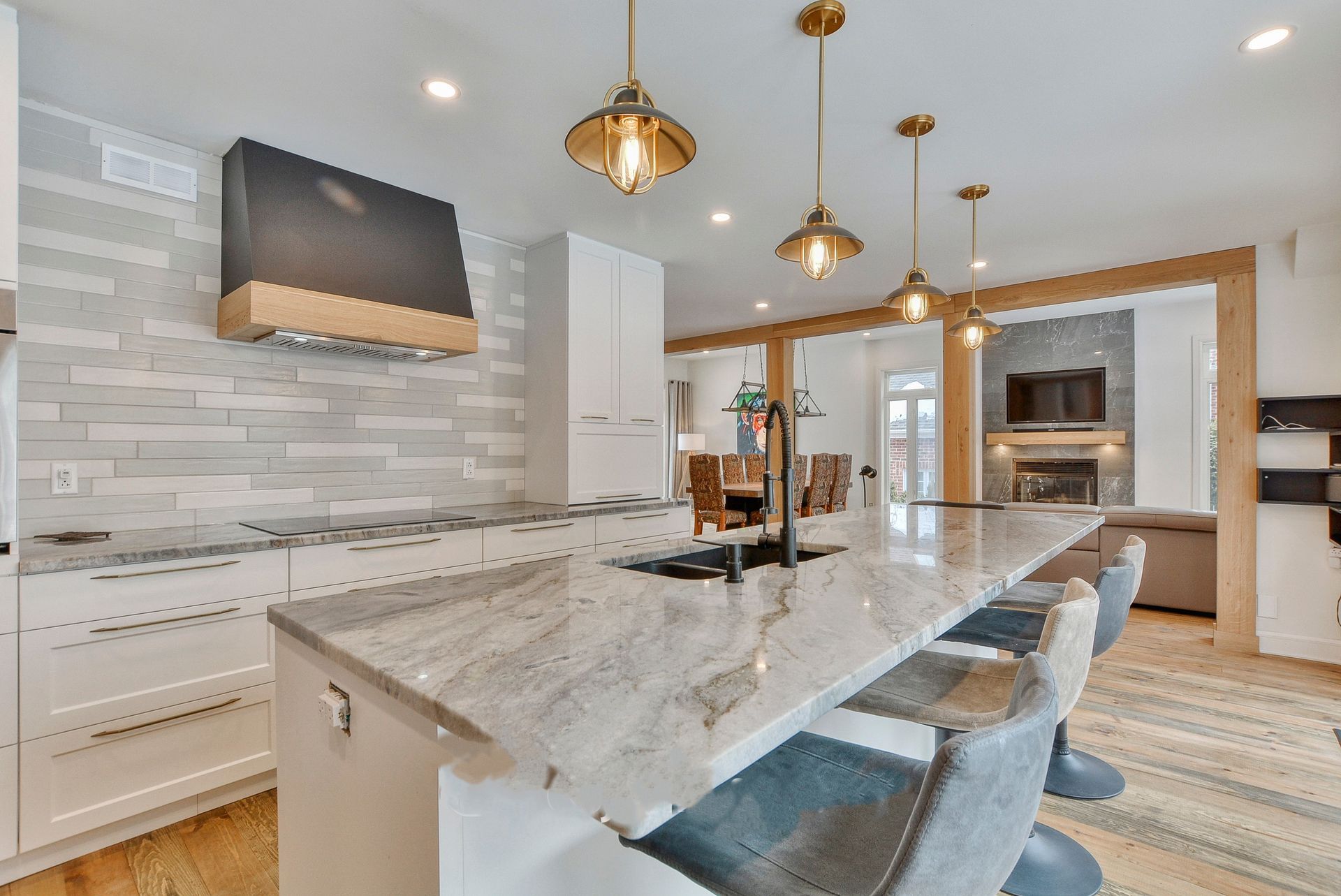 Cuisine moderne avec armoires blanches, îlot en marbre et luminaires suspendus ; vue sur le salon.