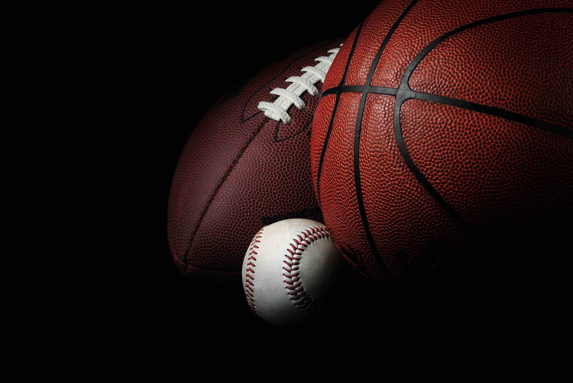A baseball and a basketball are sitting next to each other on a black background.