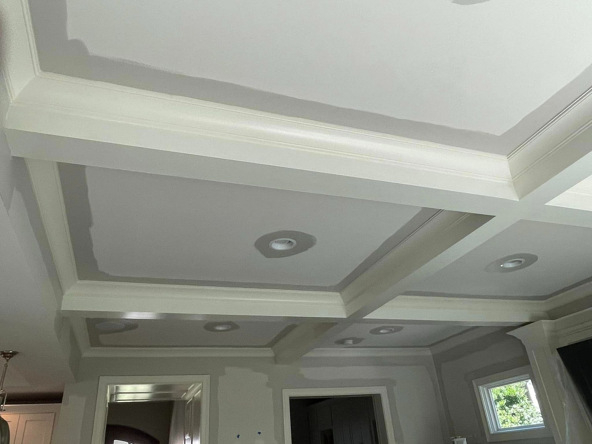 A freshly constructed white coffered ceiling with recessed lights in a room.