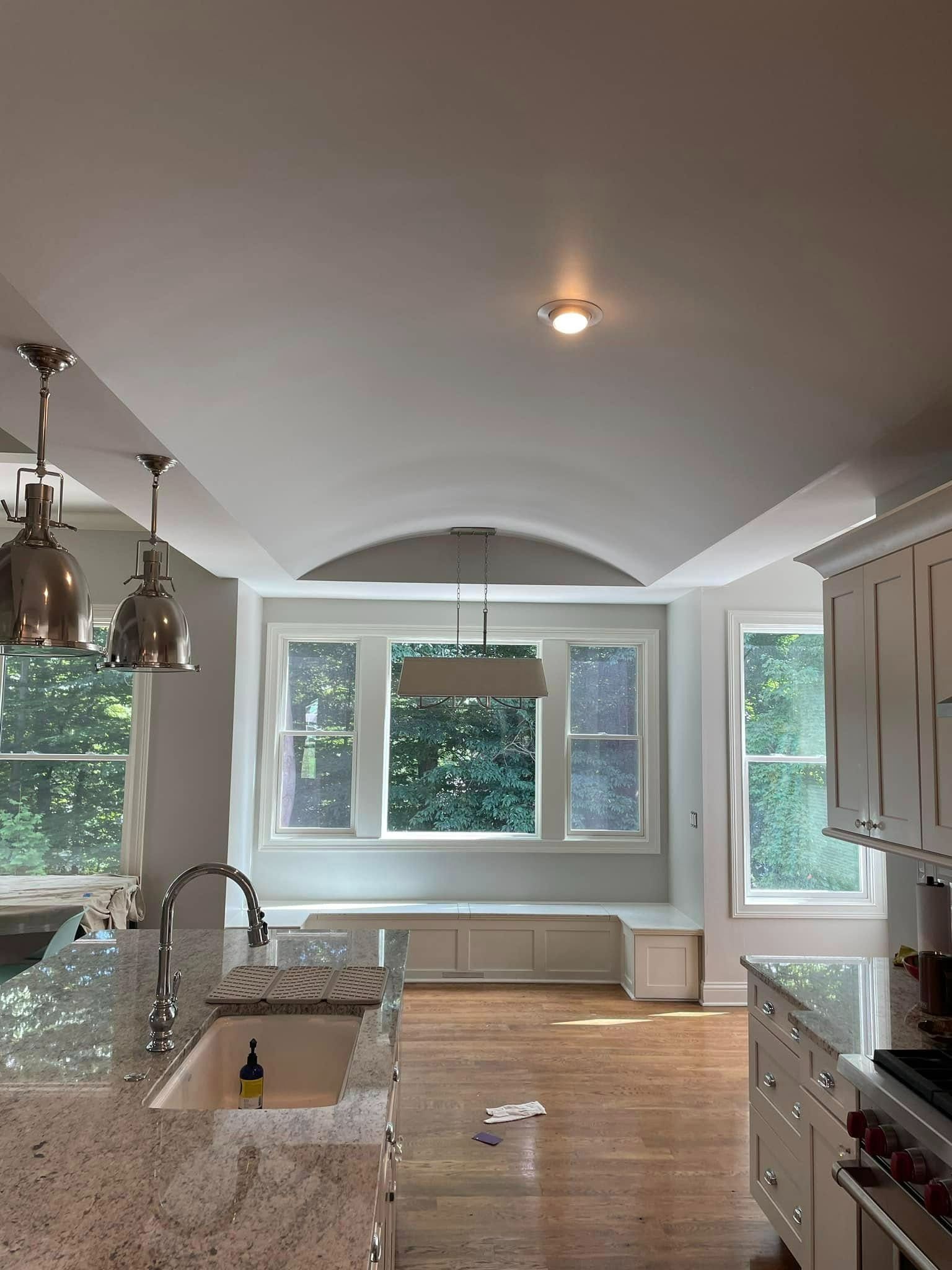 Kitchen with arched ceiling, windows, breakfast nook, pendant lights, granite countertops, and white cabinets.
