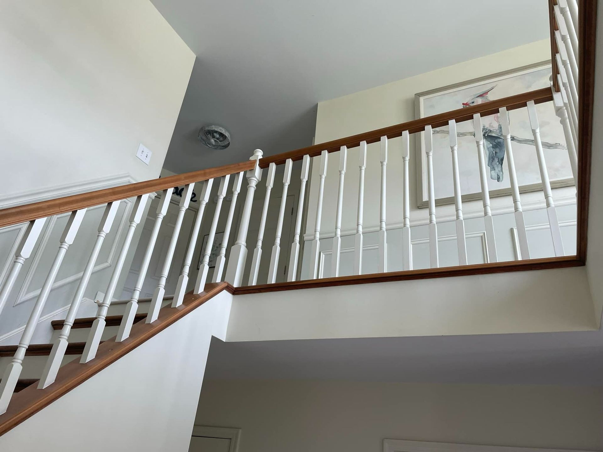 Staircase with white spindles, brown handrails, and a painting on a light-colored wall.