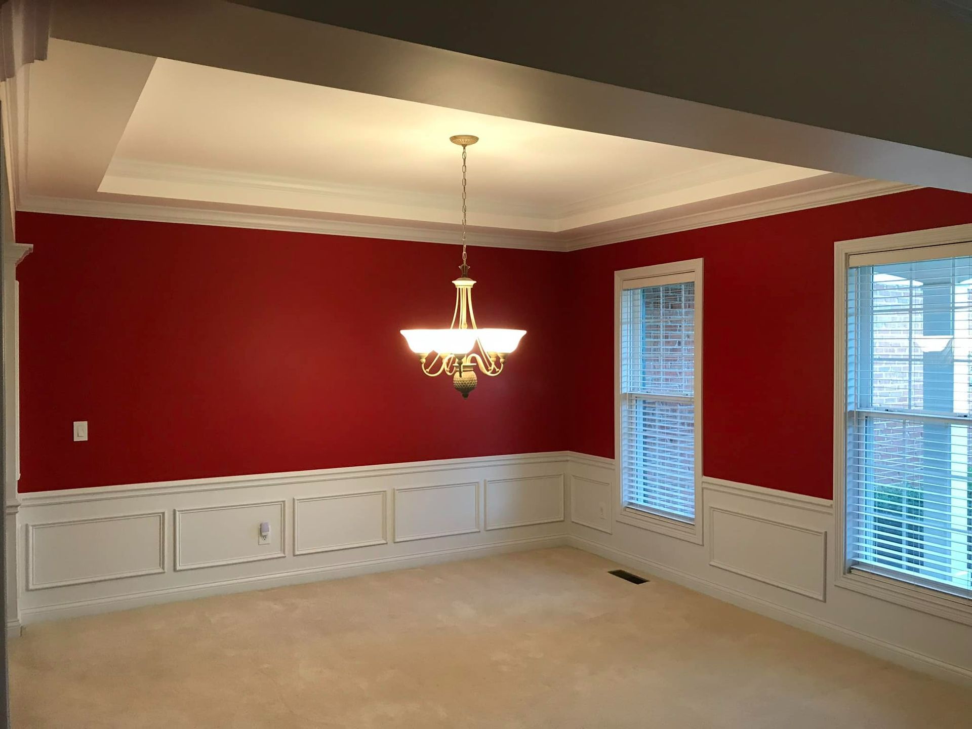 Dining room with red walls, white wainscoting, and a chandelier.