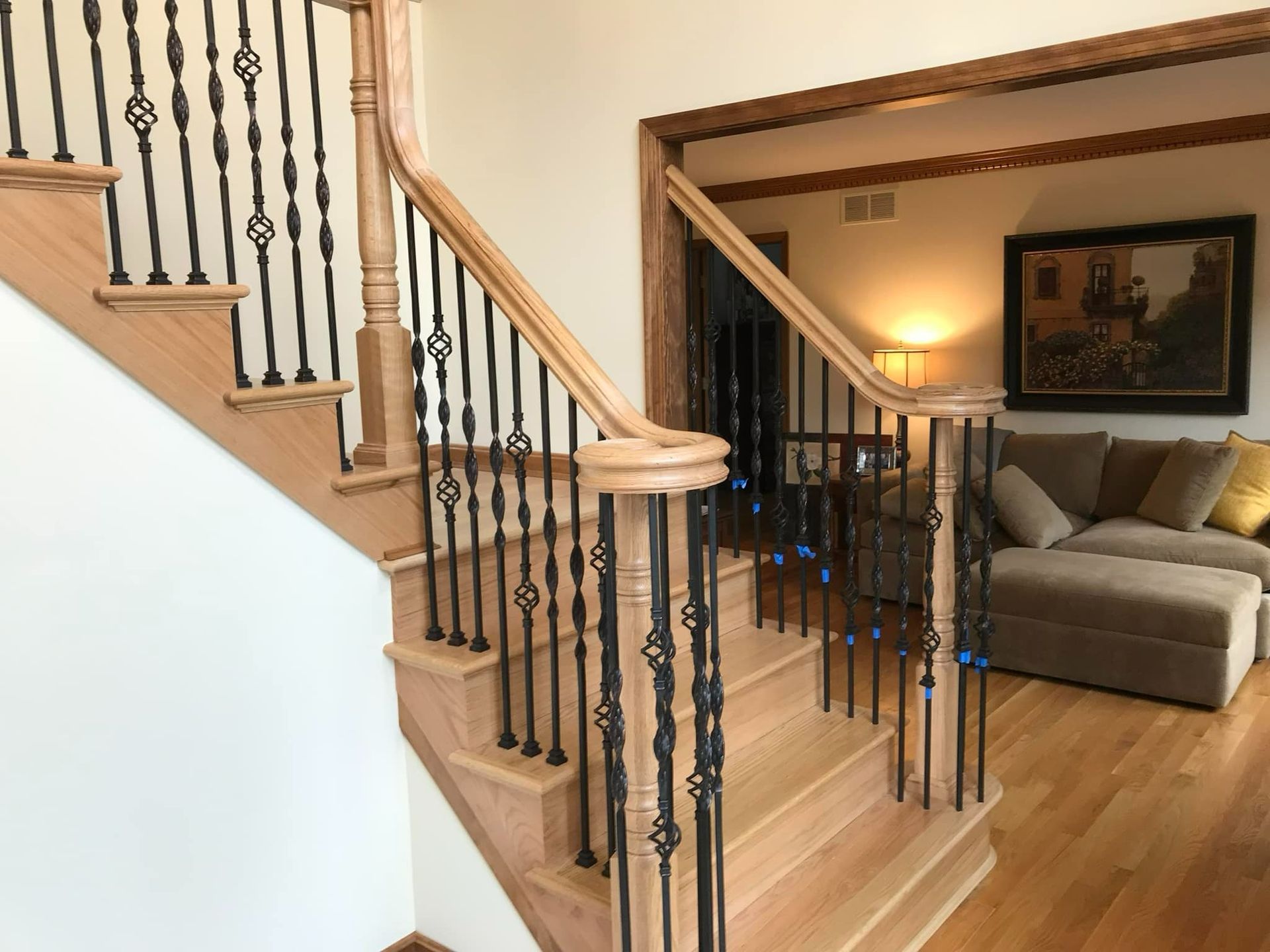 Wooden staircase with black iron balusters. Railing and steps are a light wood.