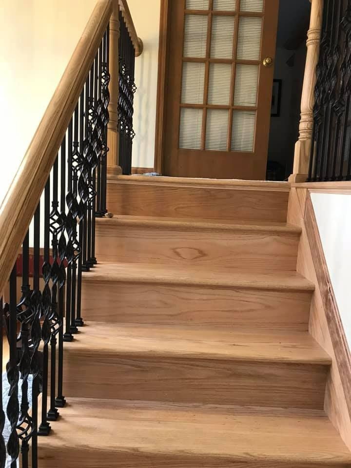 Wooden staircase with black iron railing, leading up to a light-filled doorway.