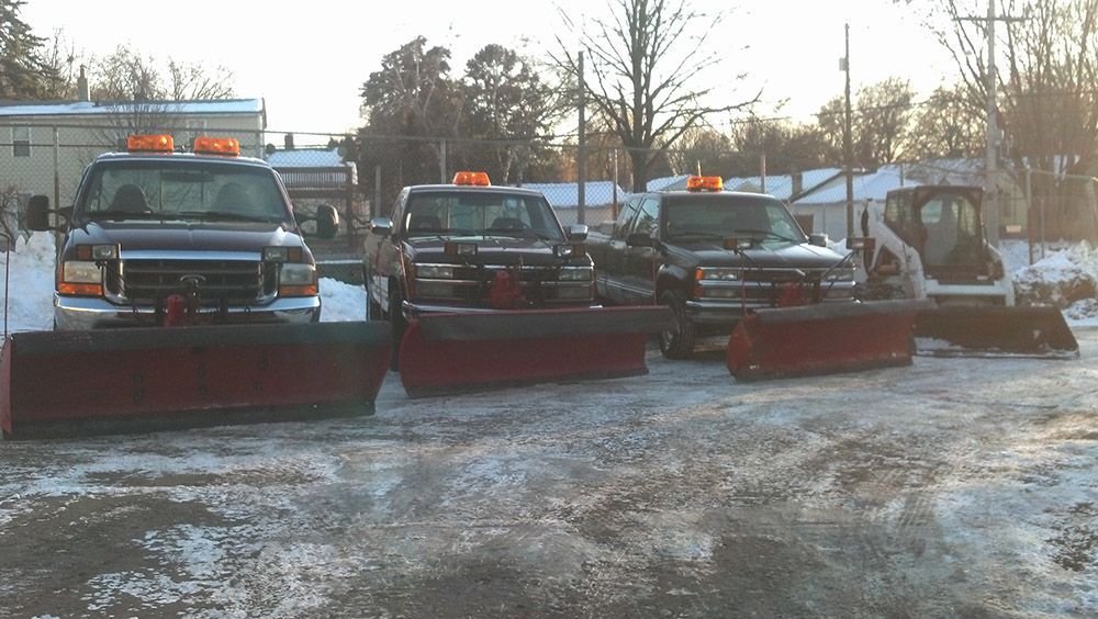 A row of snow plows are parked in a parking lot