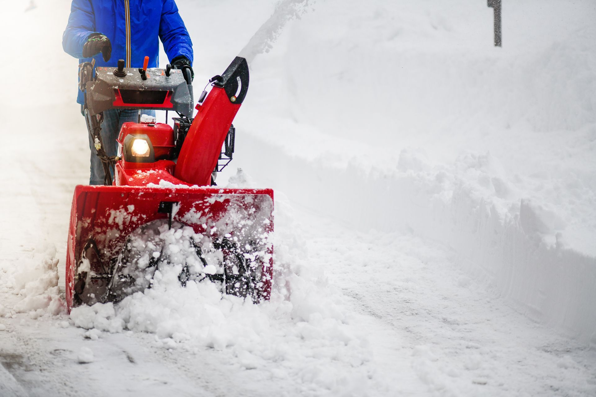 A man is using a snow blower to clear snow from the sidewalk
