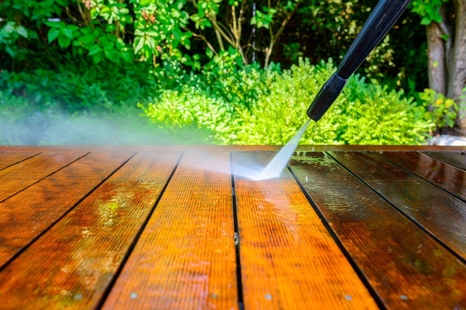 A person is using a high pressure washer to clean a wooden deck