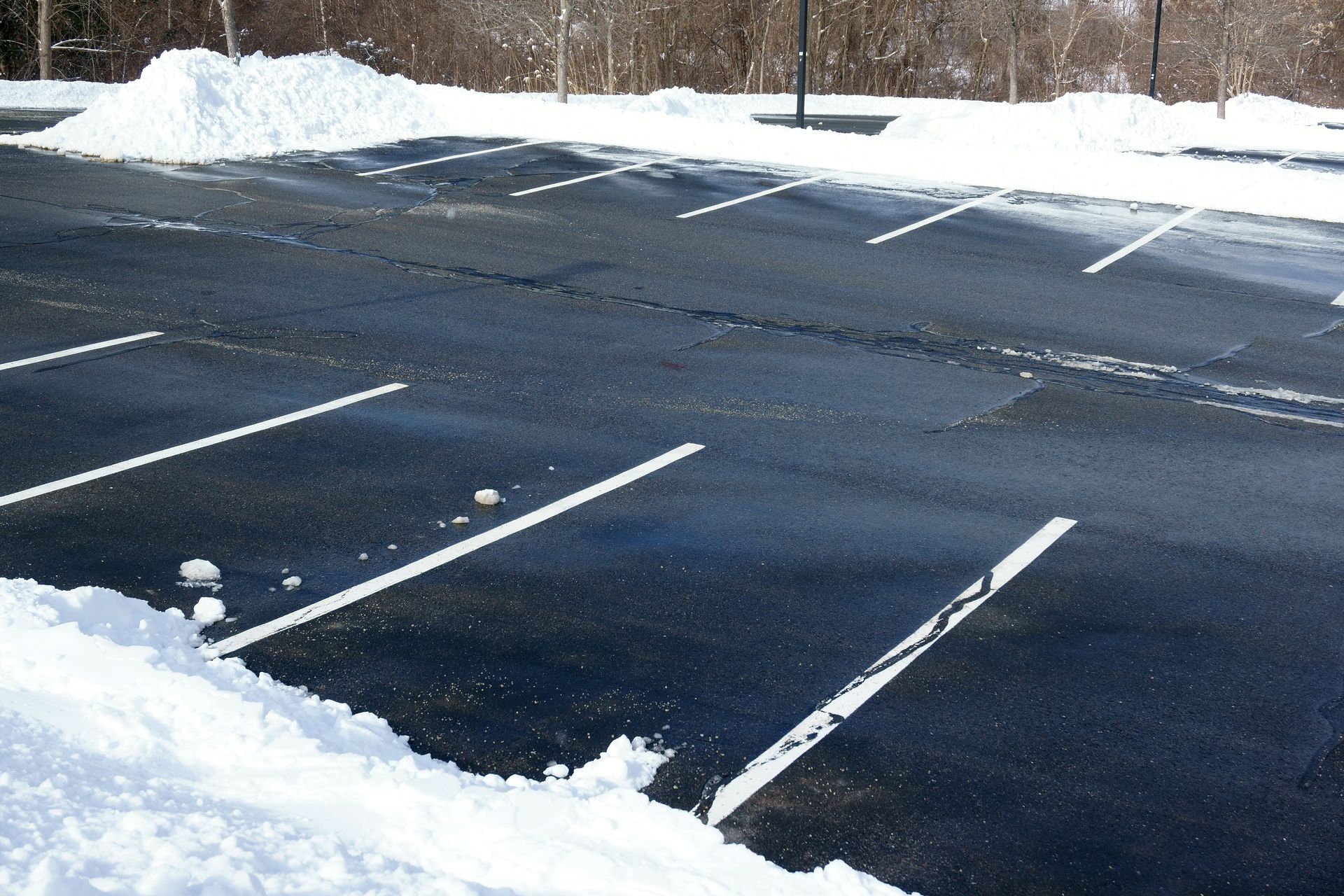 Snowy parking lot with visible white parking lines, snow piles on the sides.