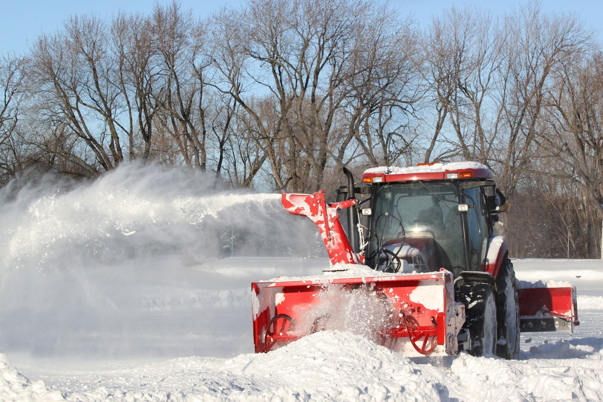 A red and white tractor is blowing snow in a snowy field