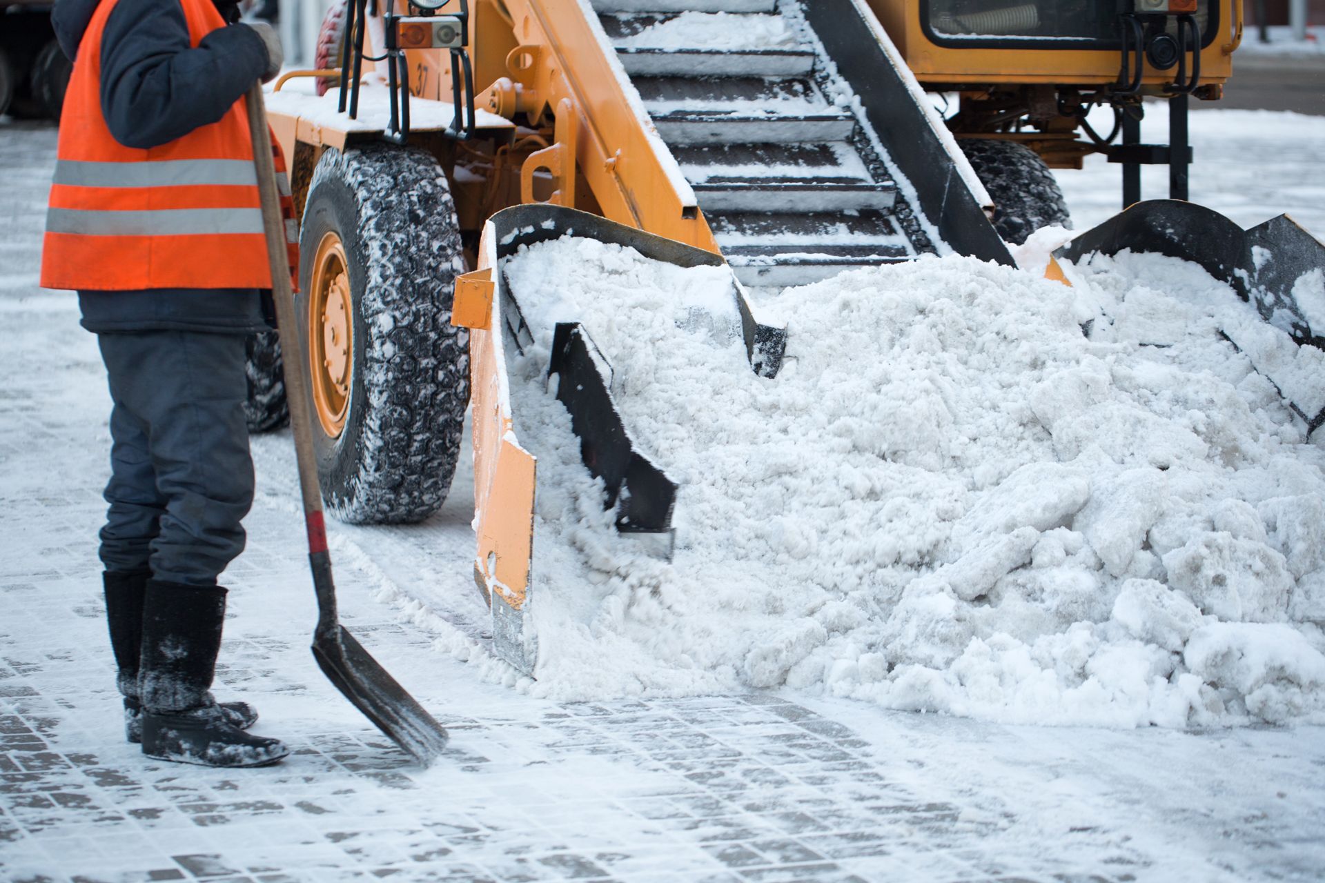 A man is shoveling snow in front of a snow plow
