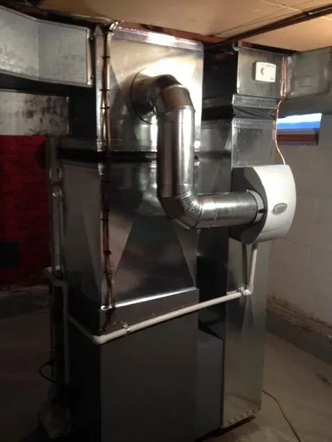 A residential furnace in a basement with a silver metal duct system, a white humidifier, and white PVC piping.