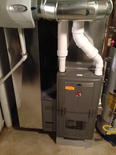 A high-efficiency gas furnace with white PVC exhaust pipes, connected to metal ductwork and a humidifier in a basement.