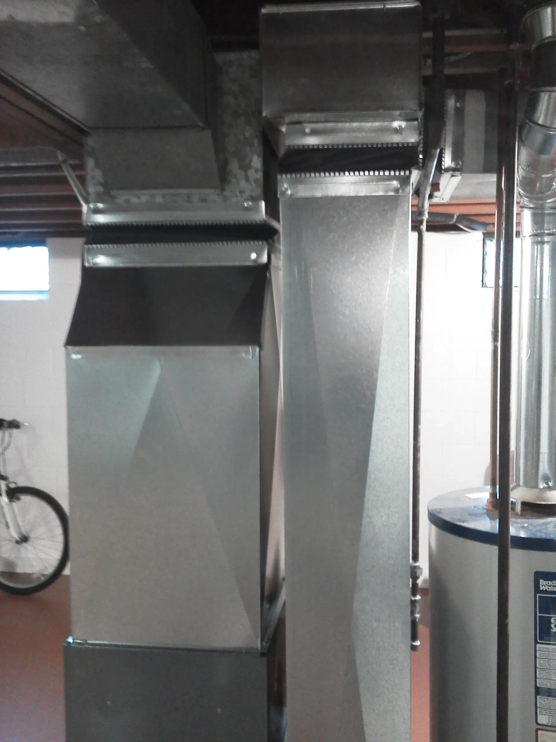Galvanized metal HVAC ductwork and a water heater installed in a residential basement.