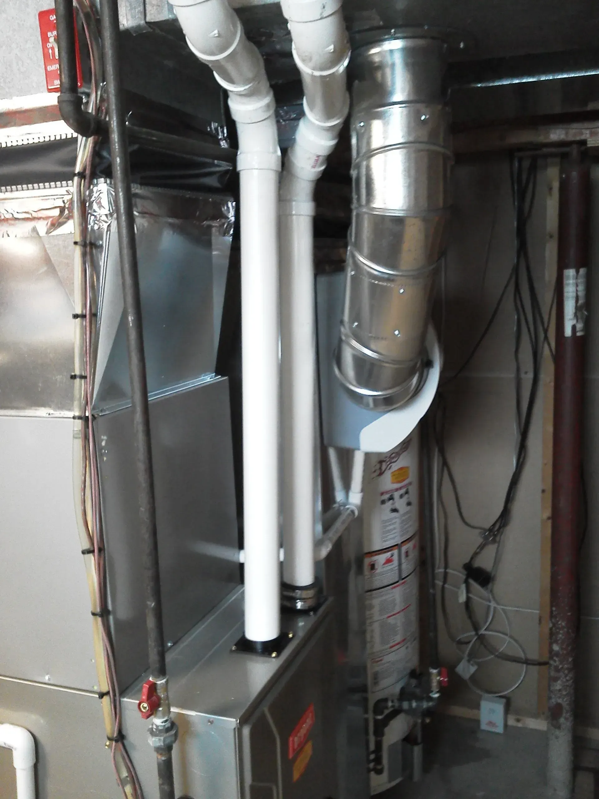 White PVC pipes and a metal exhaust flue connected to a furnace and water heater in a basement utility area.