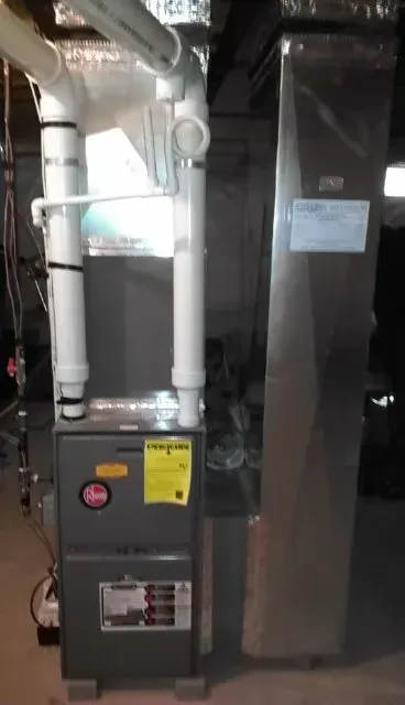 A Rheem furnace and an adjacent metal air handler unit in a residential basement setting.