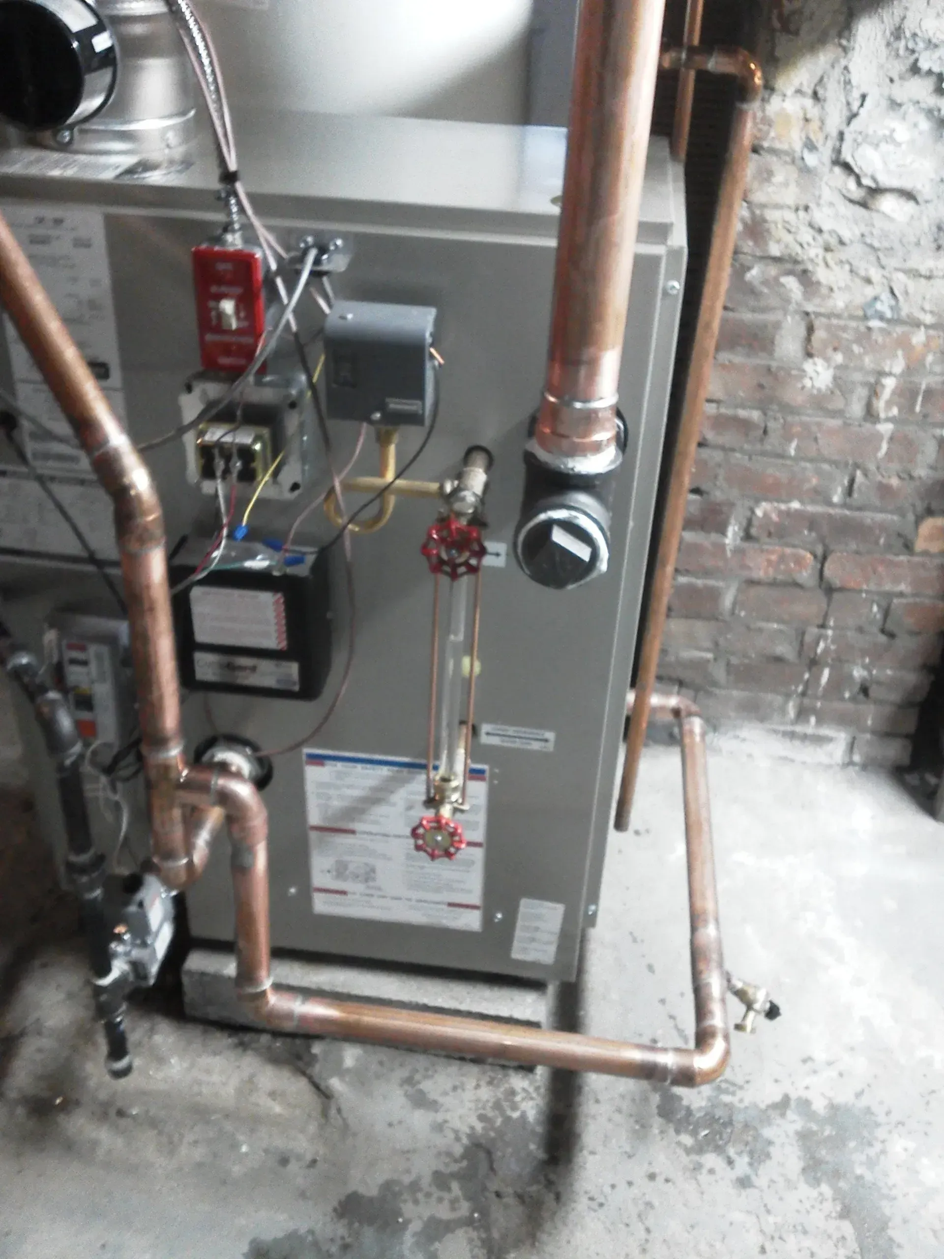 A gray boiler unit with a sight glass, copper piping, and electrical controls, located in a basement.