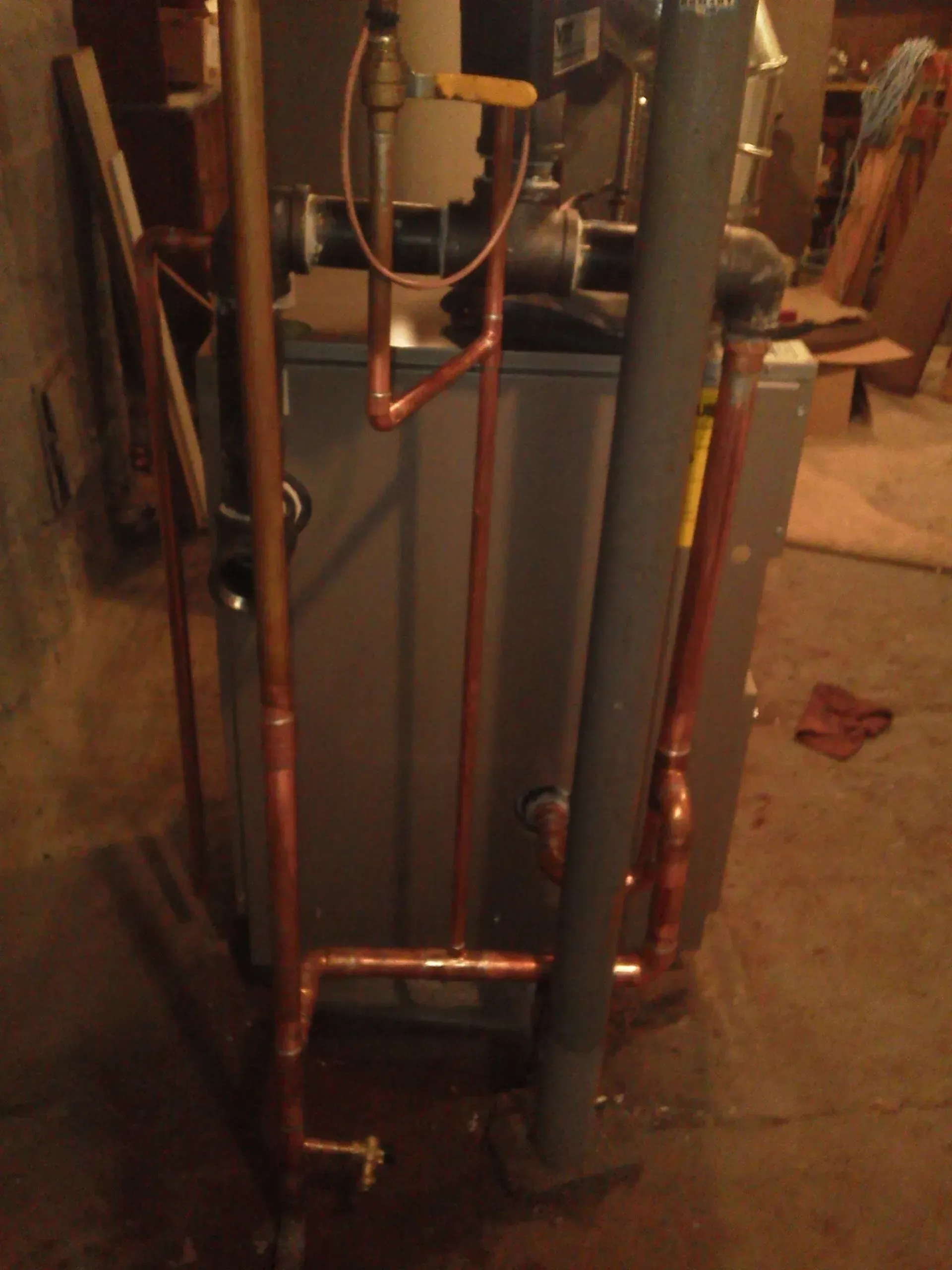 A residential boiler unit in a basement, featuring vertical copper piping and a yellow-handled shut-off valve.