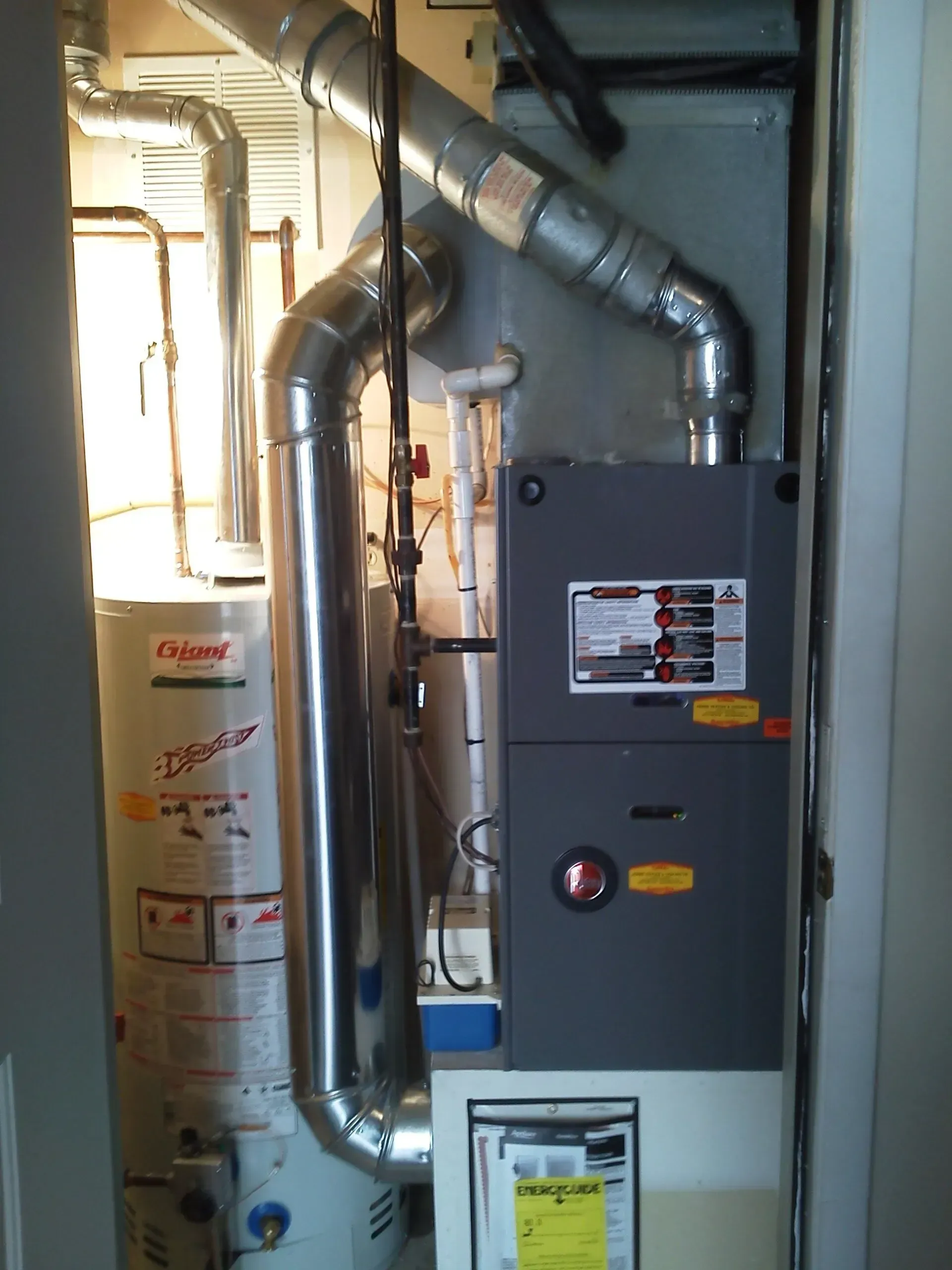A water heater and a furnace unit standing side by side in a small utility closet.