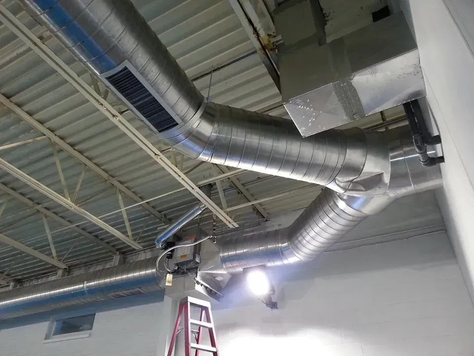 Metal HVAC ductwork suspended from a white ceiling with a ladder below.