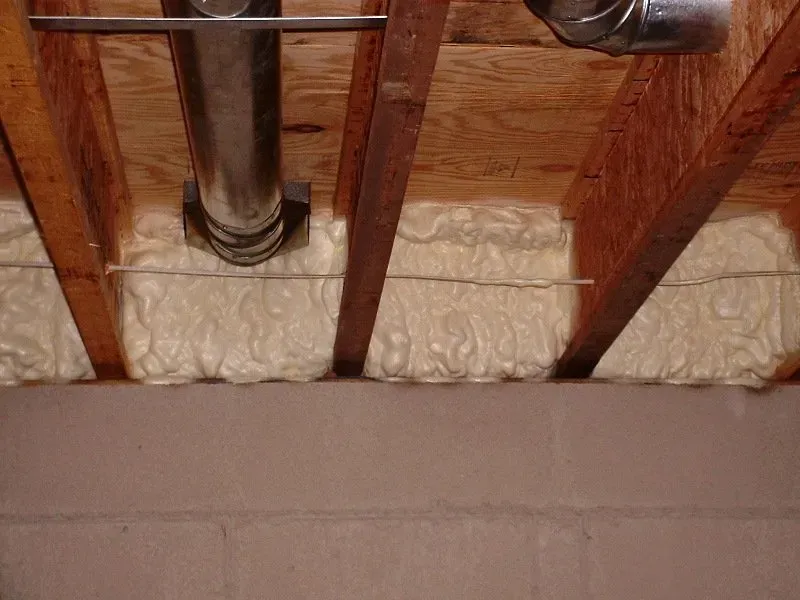 Spray foam insulation installed in the rim joist cavities above a cinder block foundation wall.