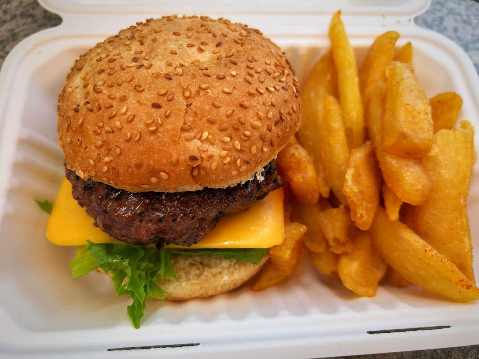 A hamburger and french fries in a styrofoam container