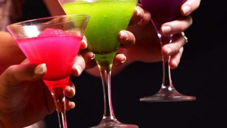 Three people are holding martini glasses with different colored liquids in them.