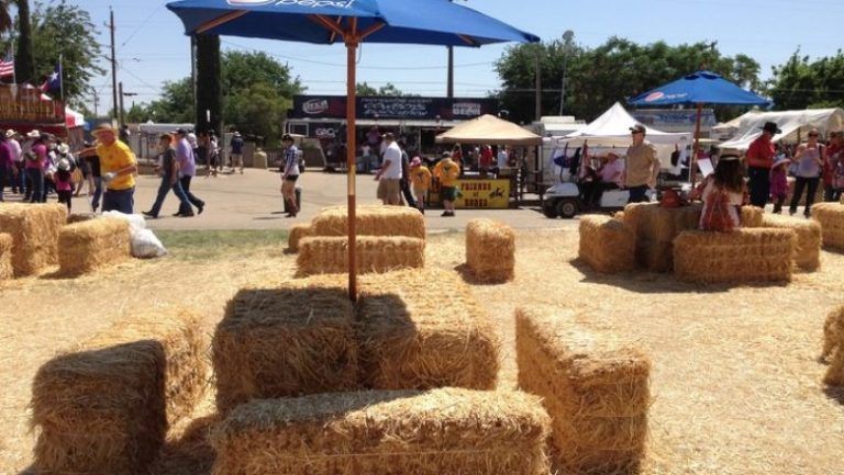 A bunch of hay bales are sitting under an umbrella in a field.