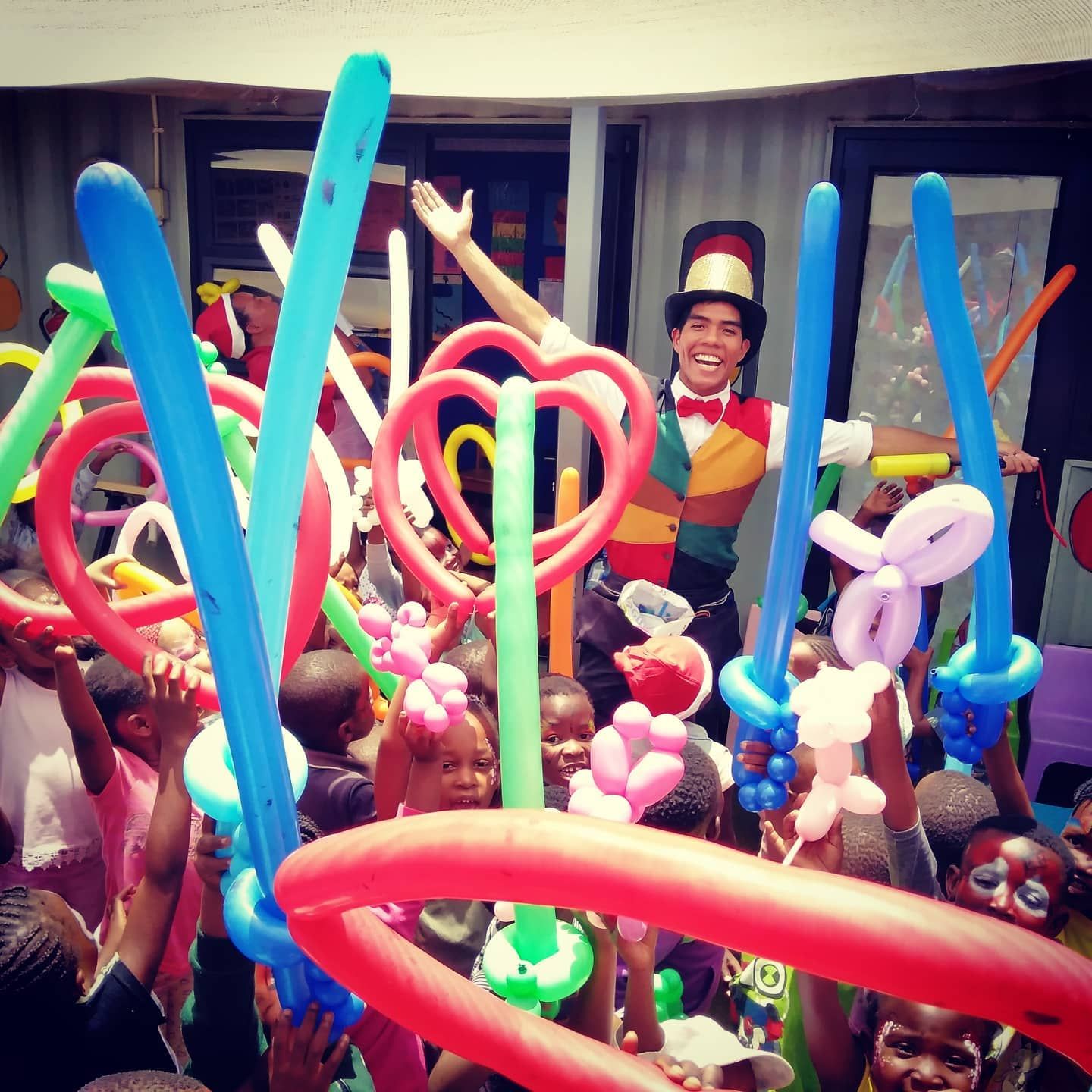 A man in a top hat is surrounded by children holding balloons