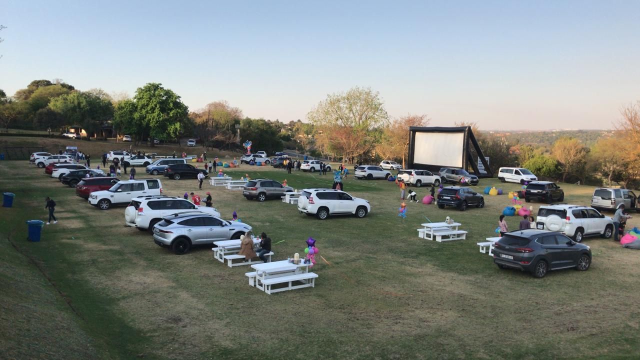 A lot of cars are parked in a field in front of a large screen.
