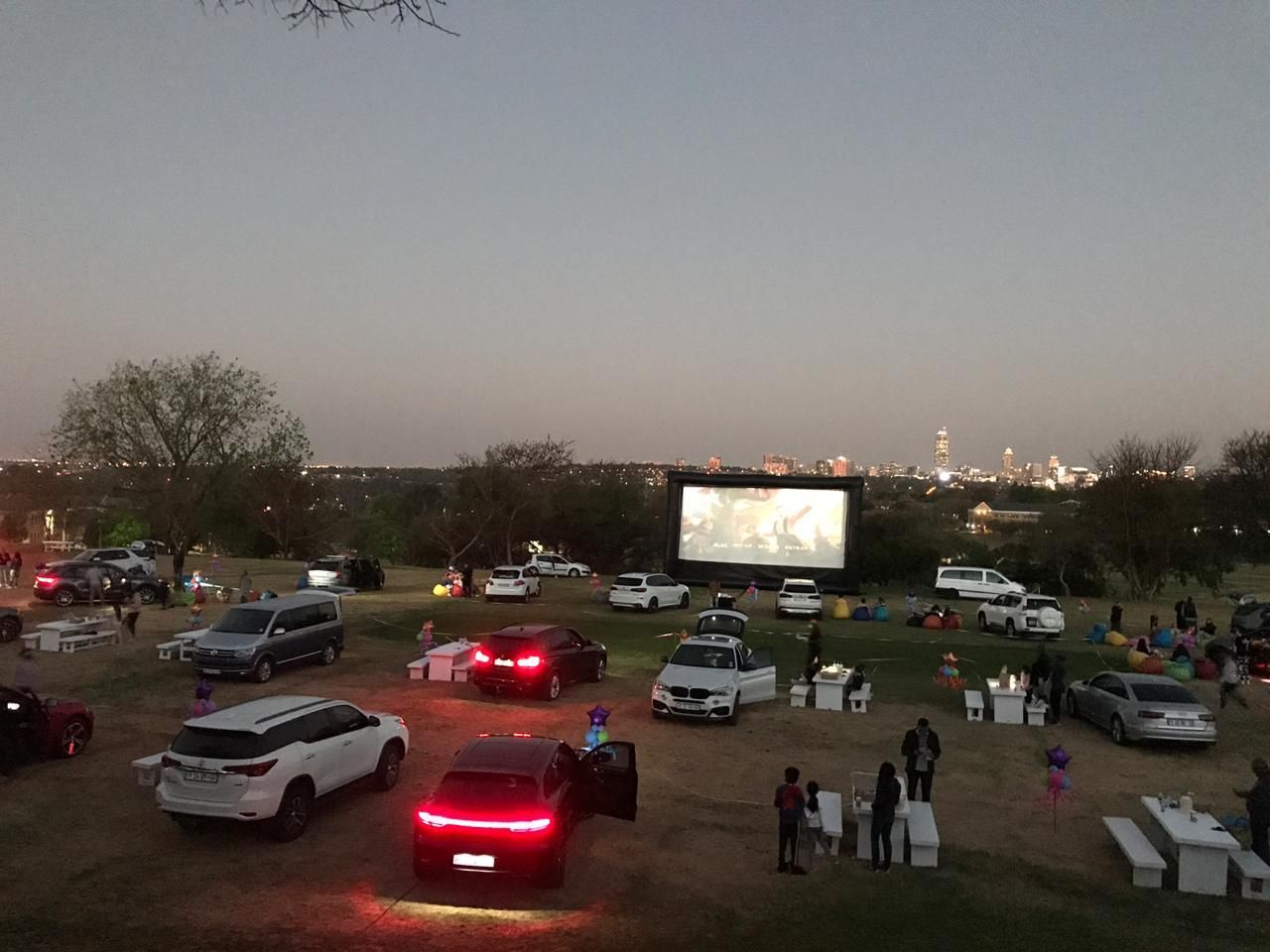 A group of cars are parked in a field in front of a large screen.
